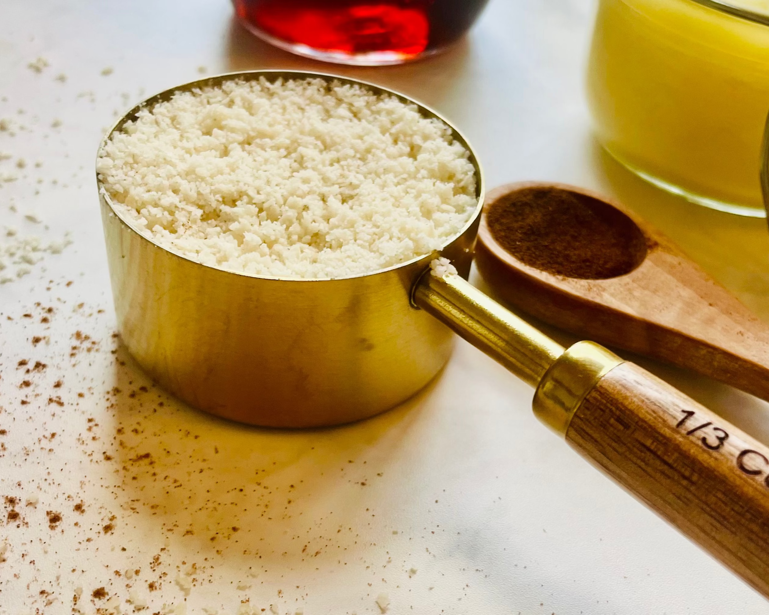 Measuring cup with flour on a surface with a jar of oil and glass container in the background.