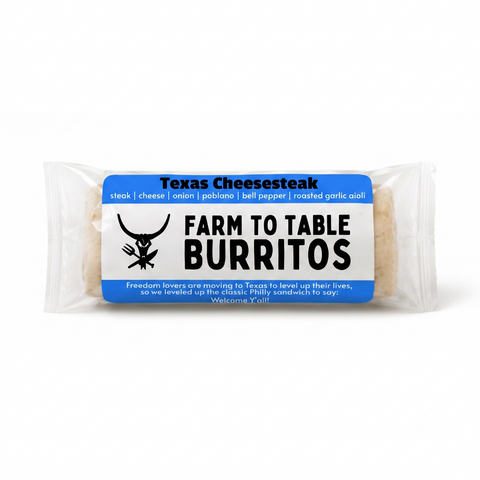 A packaged burrito on a clean white background. The clear plastic wrapper shows a round burrito with a blue and white paper label that reads 'Texas Cheesesteak' and 'FARM TO TABLE BURITOS' with a black steer logo.
